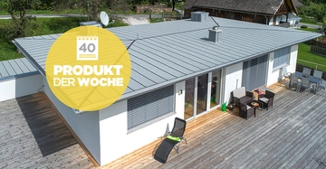 Ein flaches Wohnhaus mit grauem Dach und großer Terrasse mit Gartenmöbeln steht in grüner Umgebung. Ein gelbes Abzeichen zeigt 40 Produkt der Woche.