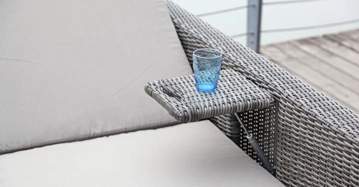Galerie-Bild 10: Eine blaues Trinkglas steht auf einem geflochtenen Rattan-Beistelltisch einer Liege auf einer Holzterrasse.