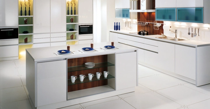 Galerie-Bild 2: Moderne weiße Küche mit Kücheninsel vier Gedecken und Regal mit Tassen Kochzeile im Hintergrund mit Oberschränken und Spüle eingerichtet mit Geräten und Dekorationen unter beleuchtetem Regal.