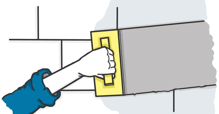 Eine Hand hält eine Kelle und streicht grauen Mörtel auf eine Wand aus weißen Fliesen.