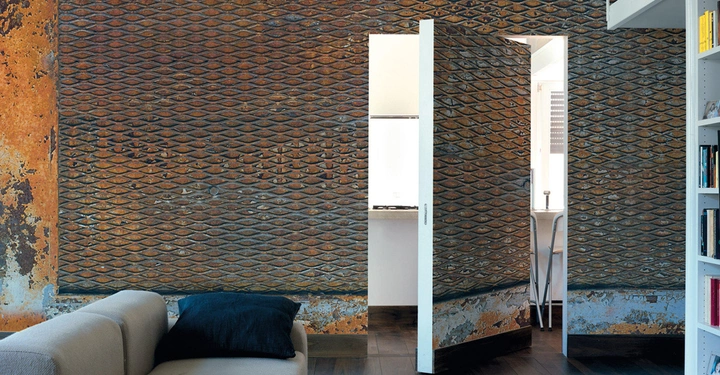 Braune Metallwand öffnet sich zu einem hellen Raum mit Kücheninventar links graues Sofa mit schwarzem Kissen rechts weiße Bücherregale