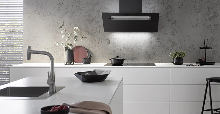 Kochfeld steht auf weißer Küchenarbeitsplatte in einer modernen Küche in Grautönen arrangiert mit minimalistischen Dekorationen wie Pflanzen und Geschirr im Hintergrund. Ein Wasserhahn befindet sich links neben einer Spüle.