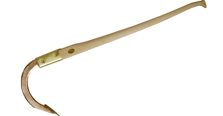 Ein Holzstab mit gebogener Metallspitze liegt in einem leeren weißen Raum.