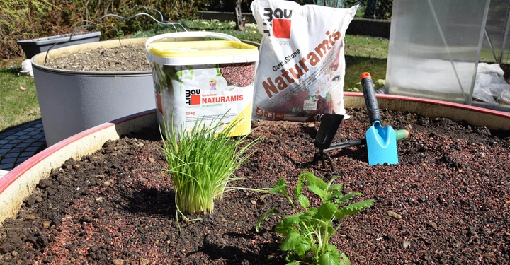 Ein Hochbeet mit frischer Erde und zwei Pflanzen Aufschrift: NATURAMIS Gartensubstrat 10 l