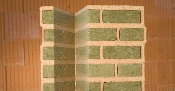 Abschnitt einer isolierten Ziegelwand steht gerade aufrecht in Richtung Betrachter beige und grün vor einer unfokussierten zweiten Ziegelwand im Hintergrund