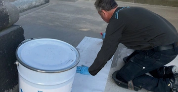 Bauarbeiter hockend am Boden verarbeitet ein Triflexprodukt für Abdichtung.