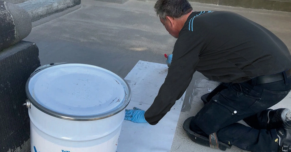 Bauarbeiter hockend am Boden verarbeitet ein Triflexprodukt für Abdichtung.