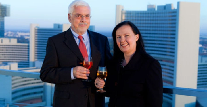 Galerie-Bild 11: Ein Mann und eine Frau halten Weingläser in der Hand und stehen auf einem Balkon vor einer Großstadtskyline mit modernen Hochhäusern im Hintergrund.