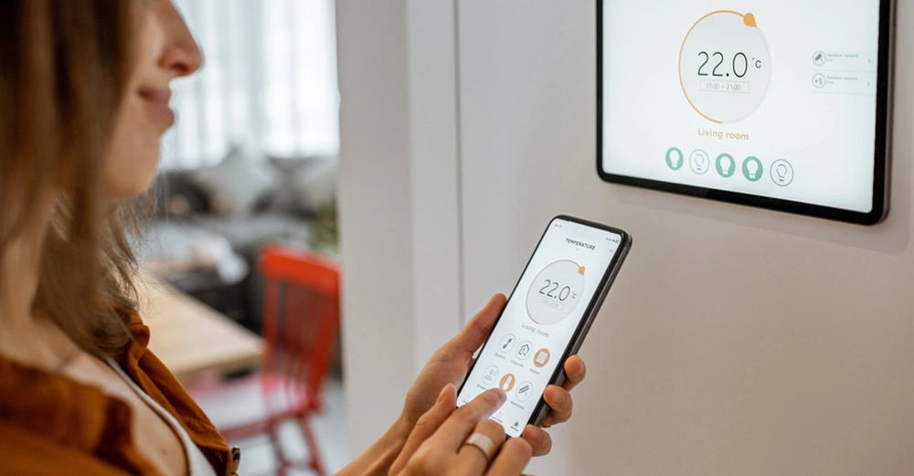 Zufrieden lächelnde Frau mit Smart Home Bedienung stellt die Wärme der Heizung im Gebäude ein.