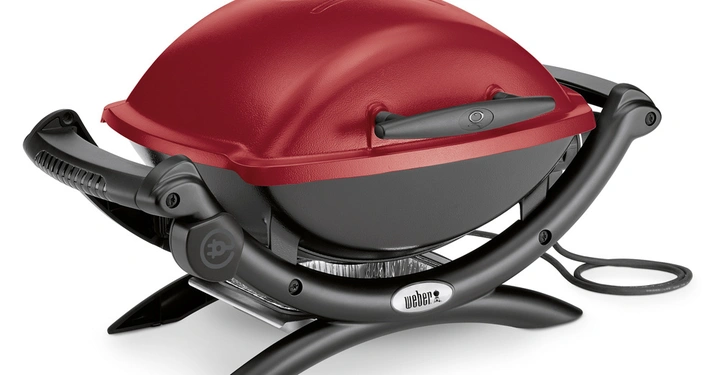 Galerie-Bild 11: Roter tragbarer Elektrogrill von Weber stehend auf einem Tisch mit geschwungenem schwarzen Ständer und integriertem Griff Text: Weber.
