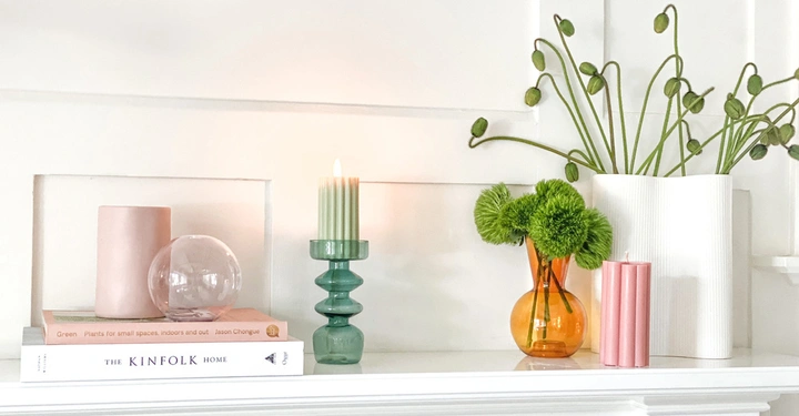 Kerzen und Blumenarrangements stehen auf einem weißen Regal in einem Wohnzimmer. Bücher mit den Titeln Green Plants for small spaces indoors and out Jason Chongue und The Kinfolk Home liegen daneben.