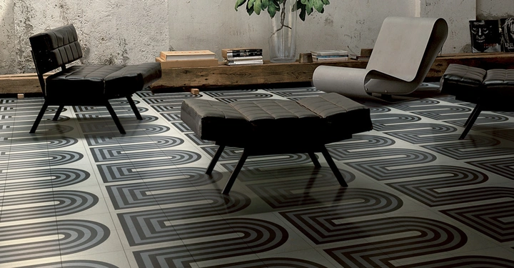 Galerie-Bild 2: Schwarzer gepolsterter Stuhl und Hocker stehen auf einem gemusterten Fliesenboden neben einem modernen weißen Stuhl in einem Raum mit rustikaler Betonwand Pflanzen und Holzbank mit Büchern im Hintergrund