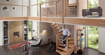 Mann geht eine moderne Holztreppe hinunter im Wohnzimmer mit großen Fenstern Büchern Kamin und Möbeln Helle und gemütliche Atmosphäre mit Blick auf den Garten.