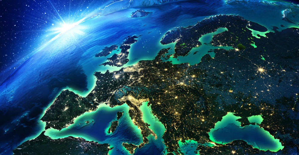 Erde zeigt Europa in der Nacht leuchtend; Städte und Straßenlichter sichtbar beleuchtend; Weltraum als Hintergrund mit Sonnenaufgang am Horizont.