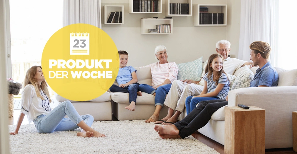 Eine Familie sitzt und unterhält sich auf einem Sofa und Teppich in einem Wohnzimmer Text Produkt der Woche 23 auf einem gelben Kreis im Vordergrund Regale an der Wand im Hintergrund