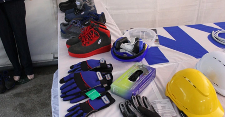 Galerie-Bild 11: Arbeitsschutzkleidung liegt auf einem Tisch in einem Zelt Arbeitsschuhe Handschuhe und Schutzhelme sind ordentlich aufgereiht umgeben von einem weißen Hintergrund und einer blauweißen Tischdecke