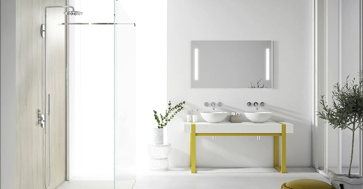 Doppelwaschbecken auf gelbem Tisch stehend neben großem Spiegel mit LED-Lichtern in modernem, minimalistischem Bad mit Glasdusche links und Pflanze rechts auf grauem Boden.