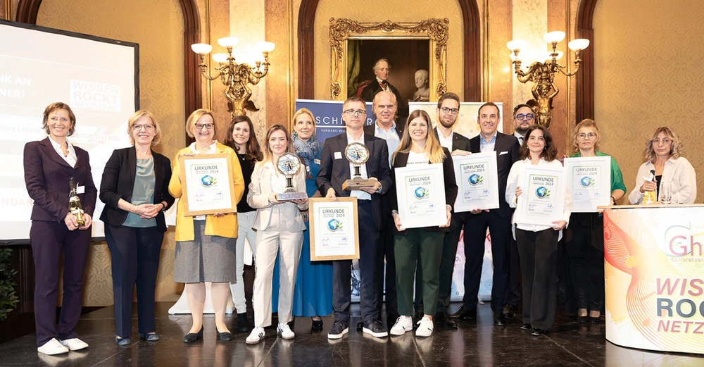 Gruppenbild von 15 Preisträgerinnen und Preisträgern mit den Urkunden in der Hand vor wunderschönem goldenen Ambiente im Palais Eschenbach.