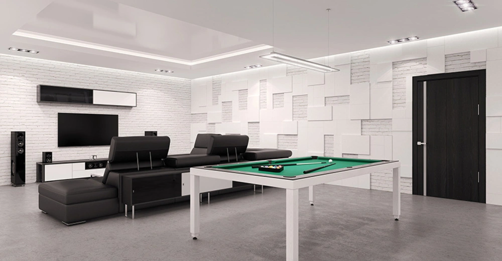 Ein Billardtisch steht in einem modernen Wohnzimmer vor einer schwarzen Ledercouch an einer Wand mit einem Flachbildfernseher und Lautsprechern helle gepolsterte Wände und eine Tür im Hintergrund