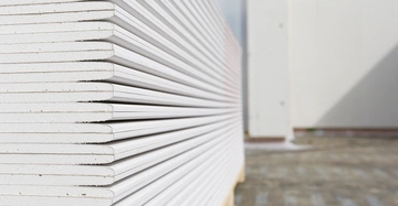 Gestapelte Gipskartonplatten liegen in der Nähe eines Gebäudes auf einem Hof aufeinander geschichtet.