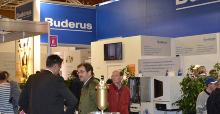 Galerie-Bild 24: Messebesucher sprechen vor einer Messestand-Ausstellung von Buderus Hallenatmosphäre und Besucher schauen sich Produkte und Displays an Schilder mit Buderus Buderus innovative Technik rund ums Haus