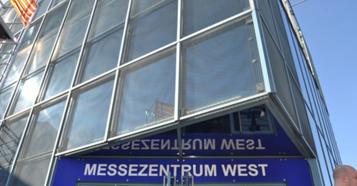 Galerie-Bild 12: Eingang eines Gebäudes mit der Aufschrift MESSEZENTRUM WEST in weißen Buchstaben über einer Glastür Der Kontext zeigt ein modernes Gebäudedesign und einen klaren Himmel