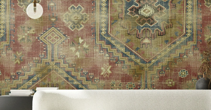 Ein cremefarbenes Sofa steht vor einer Wand mit farbenfrohem geometrischem Muster mit klassischen Ornamenten. Ein runder Couchtisch mit Schale steht davor; daneben moderne Hängelampe und Sideboard.