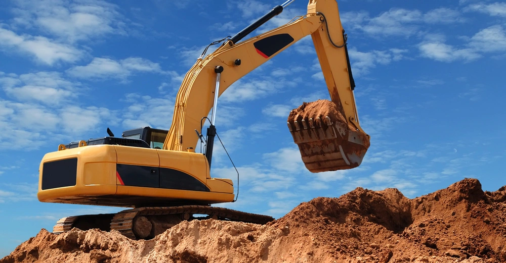 Gelber Bagger hebt Erde auf einer Baustelle in einer sandigen Umgebung bei klarem blauem Himmel