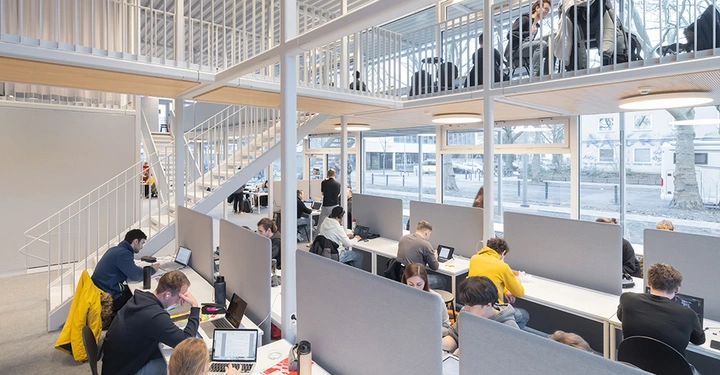 Innenaufnahme des Studentenhauses am Campus Braunschweig. Große Fensterflächen, Schreibtische und Studenten zu sehen.