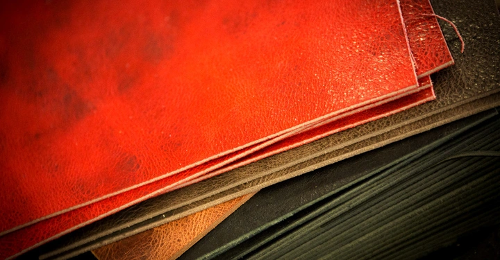 Mehrere übereinander gestapelte Lederelemente in Rot- und Brauntönen liegen in einem Atelier oder Handwerksbereich