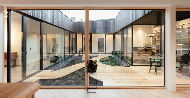 Galerie-Bild 2: Holzpfad schlängelt sich durch modernen Innenhof Garten mit Pflanzen und großen Fenstern; drinnen Esszimmer und Schreibtisch in hellem Raum