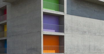 Betongebäude mit Balkonen in verschiedenen Farben grün lila orange im Vordergrund gelb rot blau im Hintergrund