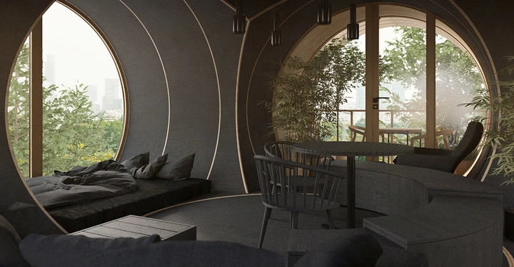 Runder Raum mit schwarzen Wänden drei großen Fenstern einem eingebauten Sofa mit Kissen einem kleinen Tisch mit Stühlen und Pflanzen außen ist eine grüne Landschaft mit Gebäuden im Hintergrund sichtbar