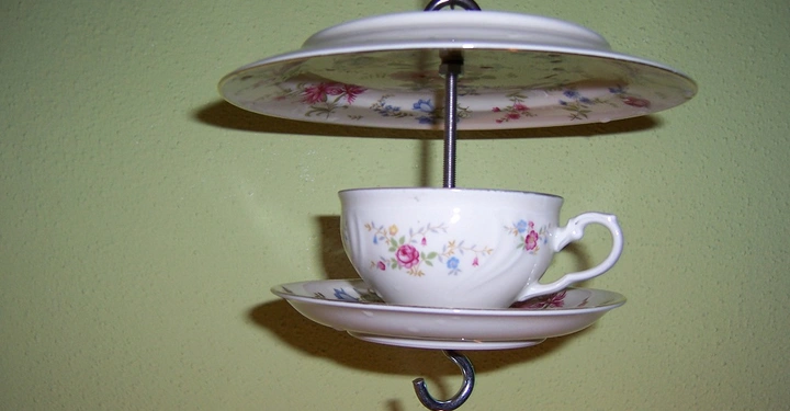 Galerie-Bild 6: Keramiktasse und -untertasse in Blumenmusterung hängen dekorativ an der Wand in einem Halter mit zwei Tellern darüber in einem olivgrünen Raum.