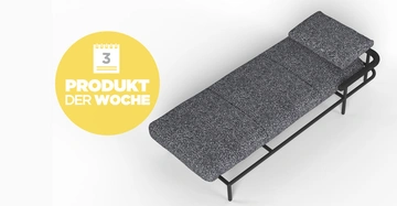Eine graue Liege steht ruhig in einem minimalistischen Raum. Ein gelbes Rundschild zeigt: 3 PRODUKT DER WOCHE