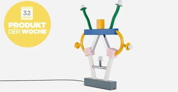 Bunte Tischlampe mit abstrakten Formen steht auf einem grauen Sockel vor einem weißen Hintergrund Links gelber Kreis mit Text Kalendersymbol 32 PRODUKT DER WOCHE