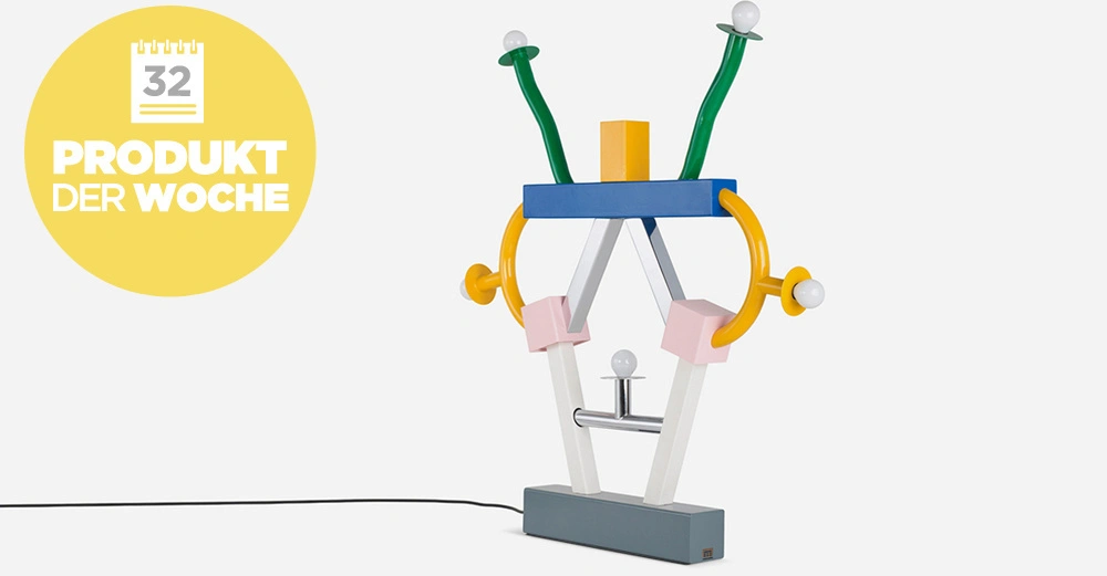 Bunte Tischlampe mit abstrakten Formen steht auf einem grauen Sockel vor einem weißen Hintergrund Links gelber Kreis mit Text Kalendersymbol 32 PRODUKT DER WOCHE