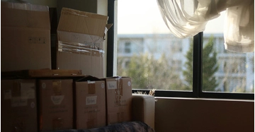 Mehrere gepackte Umzugskartons stehen in einer Wohnung neben einem Fenster.