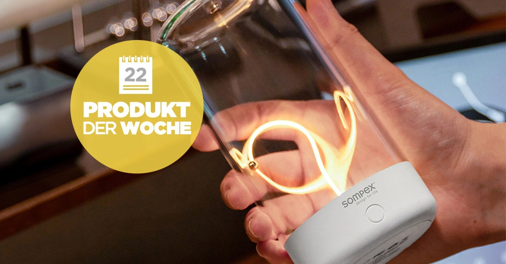 Mann hält die Sompex-Leuchte mit hell leuchtender Lichtschnur im Inneren in der Hand. Logo am Fuß der Lampe.