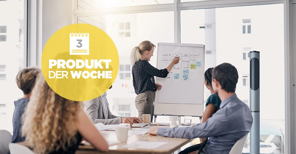 Person präsentiert Inhalte auf einem Whiteboard vor einer Gruppe von Menschen in einem Konferenzraum mit großen Fenstern. Text: 3 PRODUKT DER WOCHE.