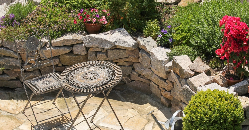 Mediterraner Garten mit Steinplatten, einer Steinmauer, mediterranen Topfpflanzen und kleines Metalltisch mit passendem Stuhl, alles aus Vogelperspektive