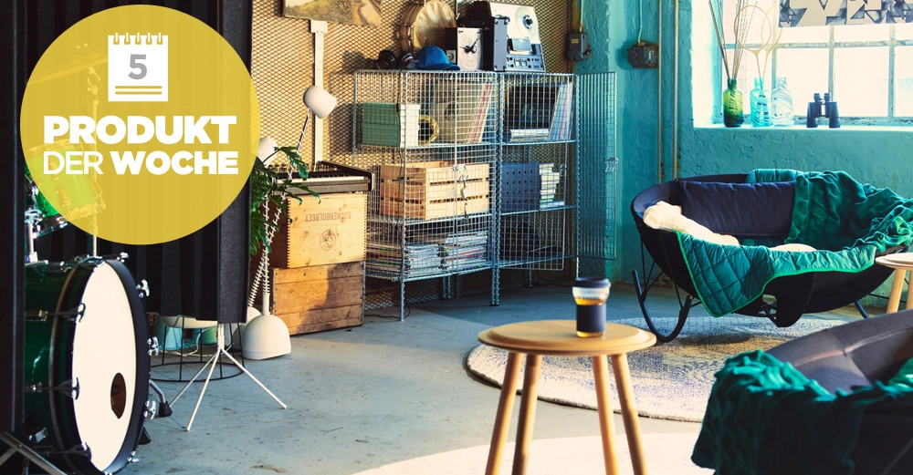 Runder Holztisch mit einer Tasse Kaffee in einem gemütlichen Wohnzimmerbereich mit Sesseln Regalen einer Trommel und einem großen gelben Kreis oben links mit der Aufschrift 5 PRODUKT DER WOCHE