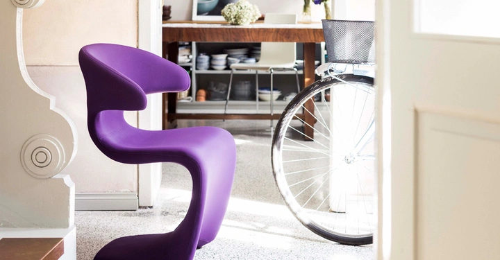 Galerie-Bild 5: Ein lila Designerstuhl steht neben einer Tür in einem hellen Esszimmer mit einer rustikalen Holztisch im Hintergrund und einem Fahrrad, das ebenfalls im Raum steht.