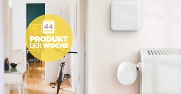 Ein Thermostat zeigt 22.6 Grad an, in einem hellen Raum mit einer Heizung darunter. Text in einem gelben Kreis lautet 44 PRODUKT DER WOCHE. Im Hintergrund ein Fahrrad und Möbel.