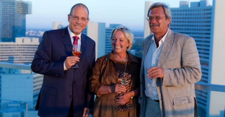 Galerie-Bild 13: Drei Personen stehen auf einer Dachterrasse und halten Getränke in der Hand. Im Hintergrund sind moderne Hochhäuser zu sehen. Die Personen lächeln und tragen elegante Kleidung.