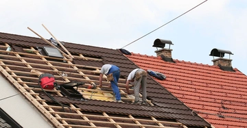 Zwei Handwerker arbeiten auf einem braunen Ziegeldach eines Hauses Kontexthintergrund sind Ziegel und zwei Schornsteine.