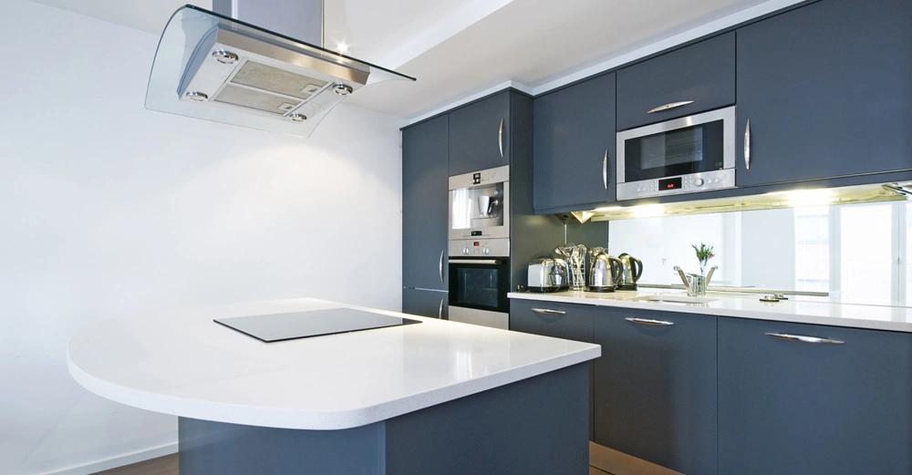 Eine moderne Küche mit dunkelgrauen Schränken Küche verfügt über einen Herd auf einer weißen Insel-Arbeitsplatte und eine eingebaute Mikrowelle und Kaffeemaschine Edelstahlkanne im Hintergrund heller Raum.