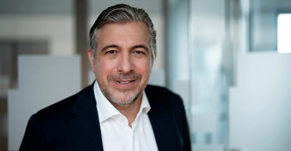 Mittelalter Mann lächelt trägt Anzug Hemd steht in modernem Büro mit Glaswänden im Hintergrund.