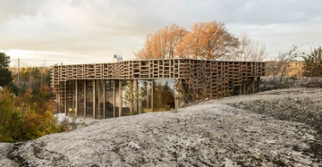 Gebäude mit einem einzigartigen Gitterdach steht inmitten einer felsigen Landschaft mit Bäumen im Hintergrund und Sonnenuntergang am Himmel