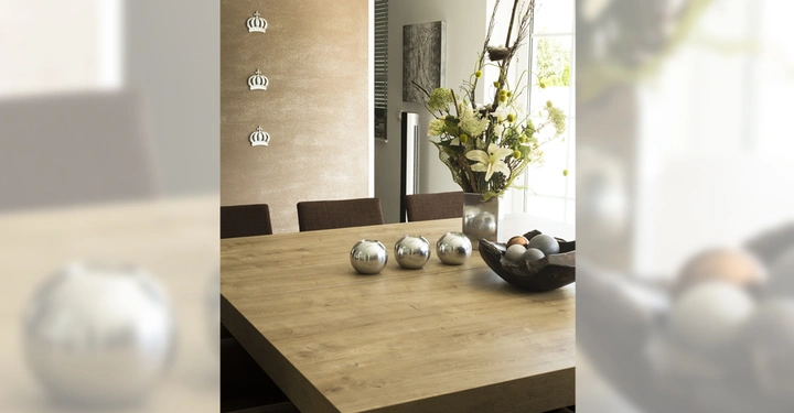 Galerie-Bild 7: Holztisch mit Metallkugeln und Blumenvase steht in modernem Speiseraum mit braunen Stühlen Wanddekoration in Form von silbernen Kronen und Fenster im Hintergrund viel Tageslicht kommt herein